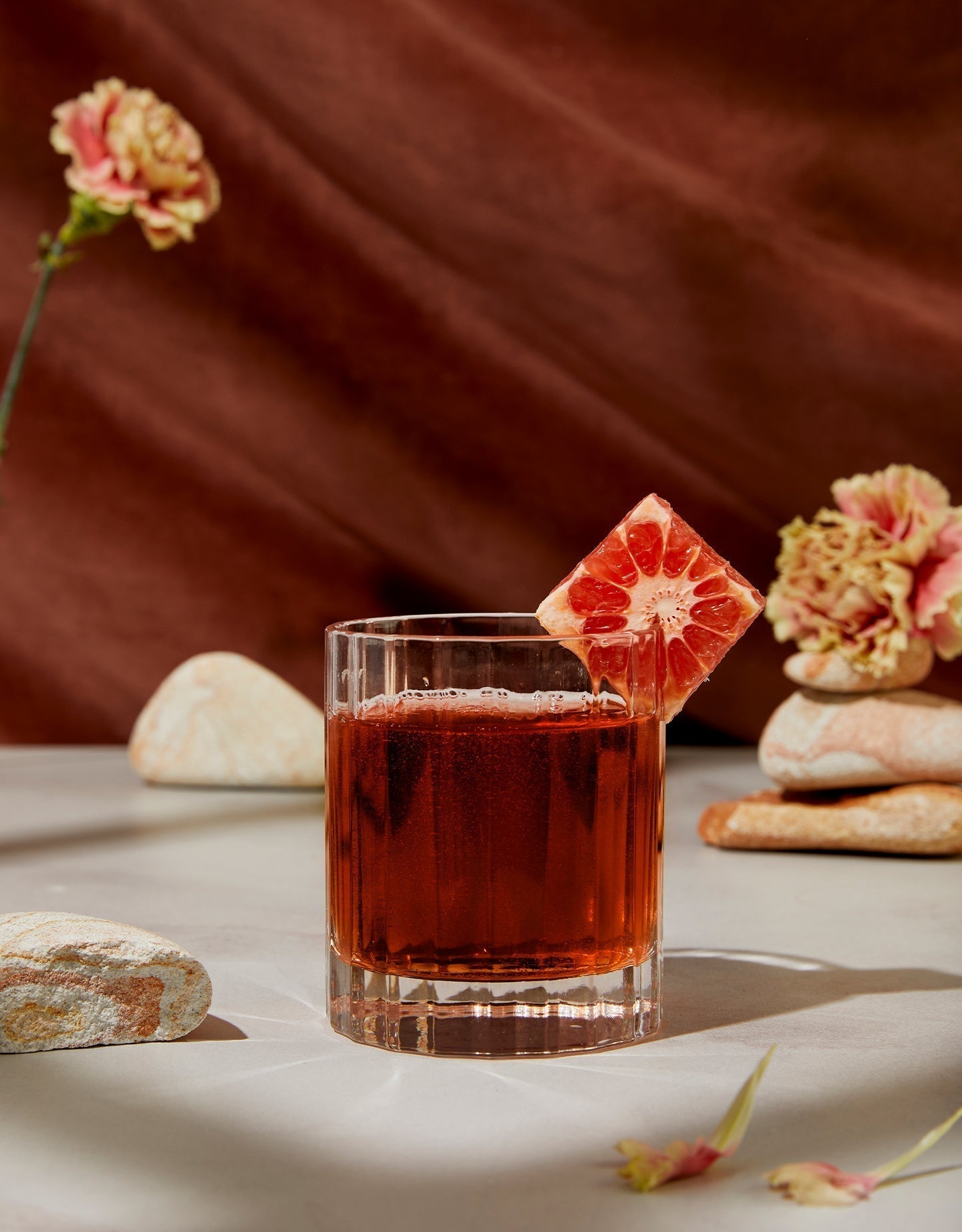 Strawberry Feels non-alcoholic cocktail garnished with grapefruit, styled with stones and carnations.