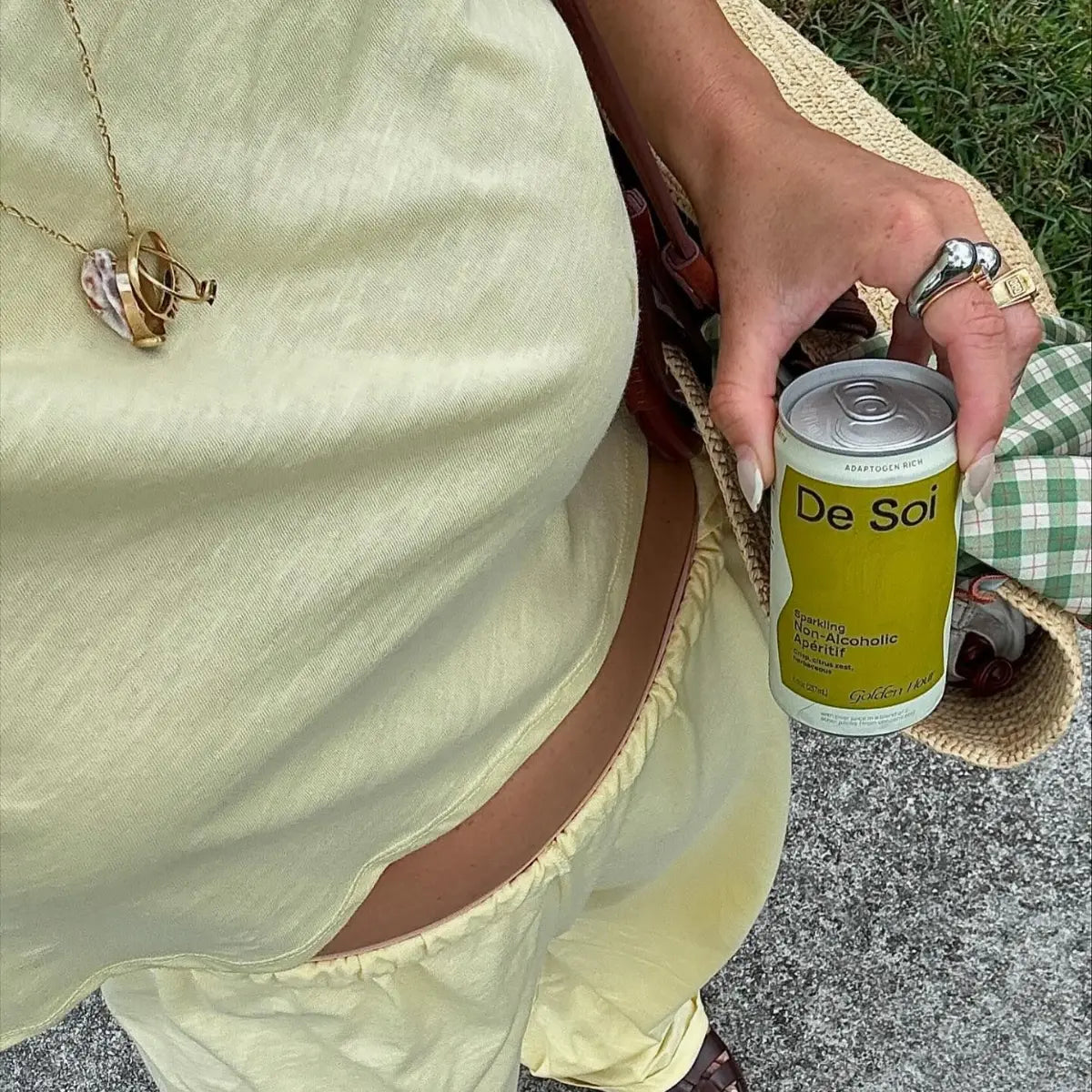 Person holding De Soi Golden Hour sparkling non-alcoholic aperitif can with straw bag.