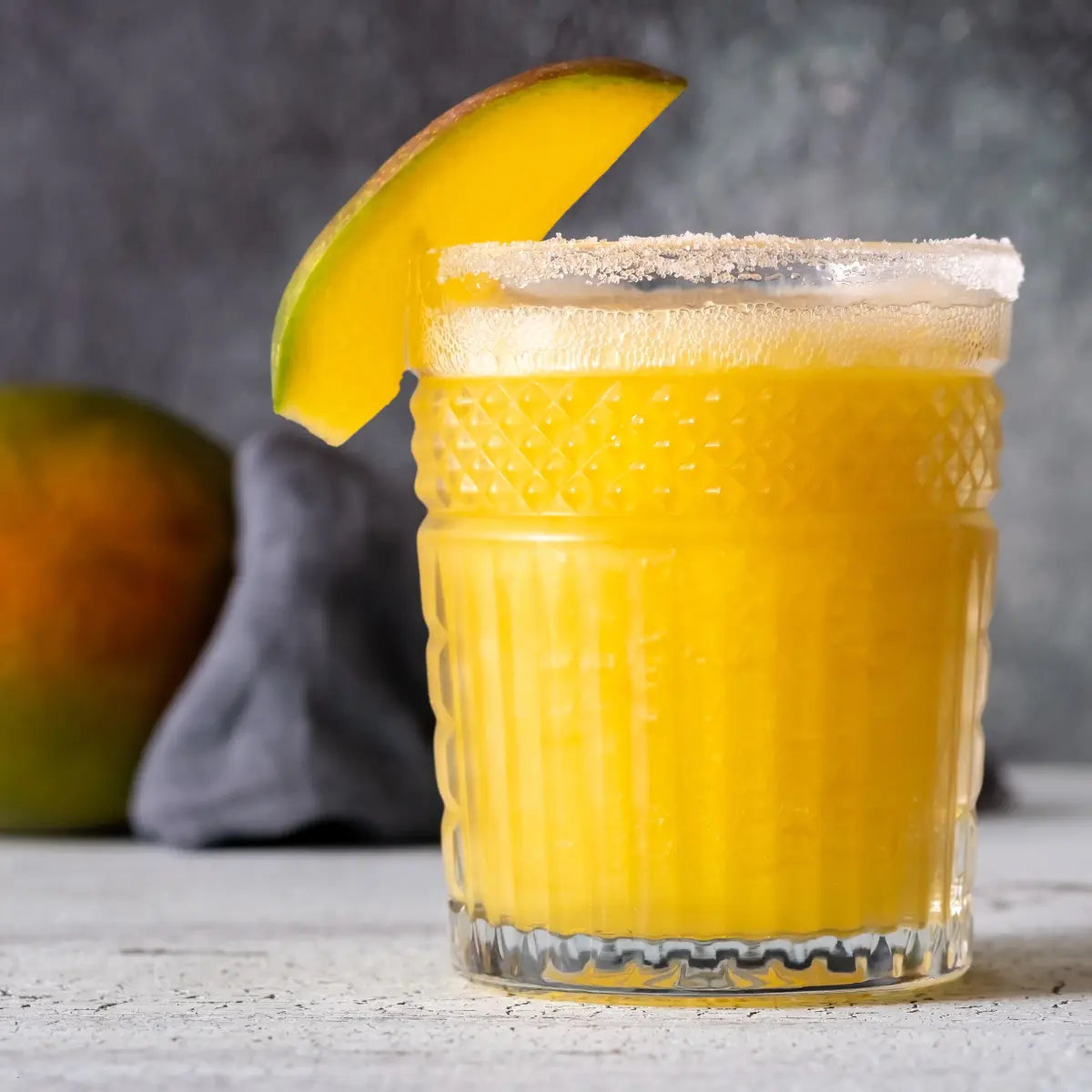 Mango mule mocktail in a textured glass with a sugared rim and a fresh mango wedge, set on a gray background
