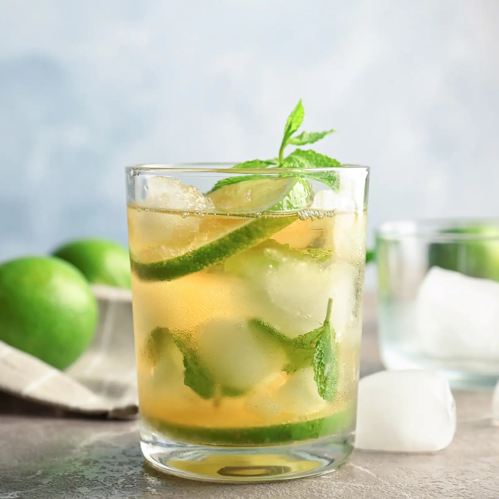 Mint Julep mocktail with lime slices and fresh mint served in a glass against a soft blue background