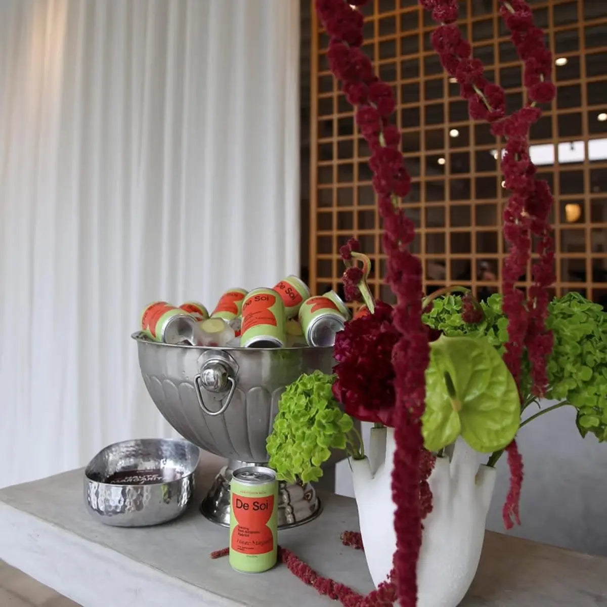 Non-alcoholic aperitif display with De Soi cans in an ice bucket next to vibrant floral arrangements.