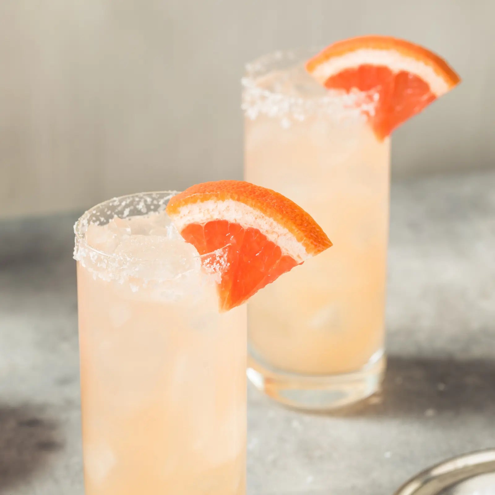 Paloma mocktail in a tall glass with salted rim and grapefruit wedge garnish on a textured surface