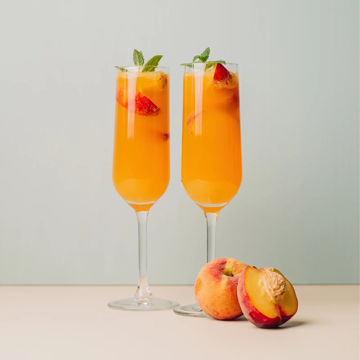 Two Peach Bellini mocktails in tall glasses with mint leaves and peach slices, next to whole peaches