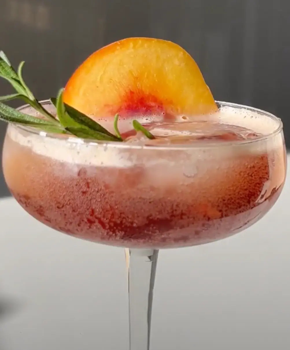 Peach mocktail in a coupe glass garnished with a peach slice and rosemary.
