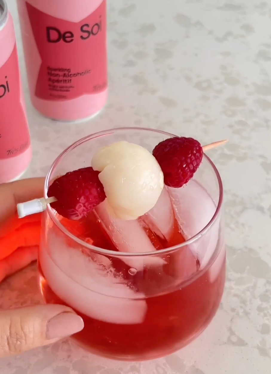 Pink De Soi Très Rosé lychee spritz garnished with raspberries and lychee on a skewer.