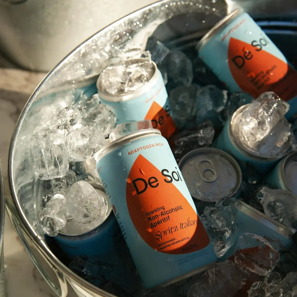 De Soi Spritz Italiano non-alcoholic aperitif cans chilling on ice in a metal bucket.