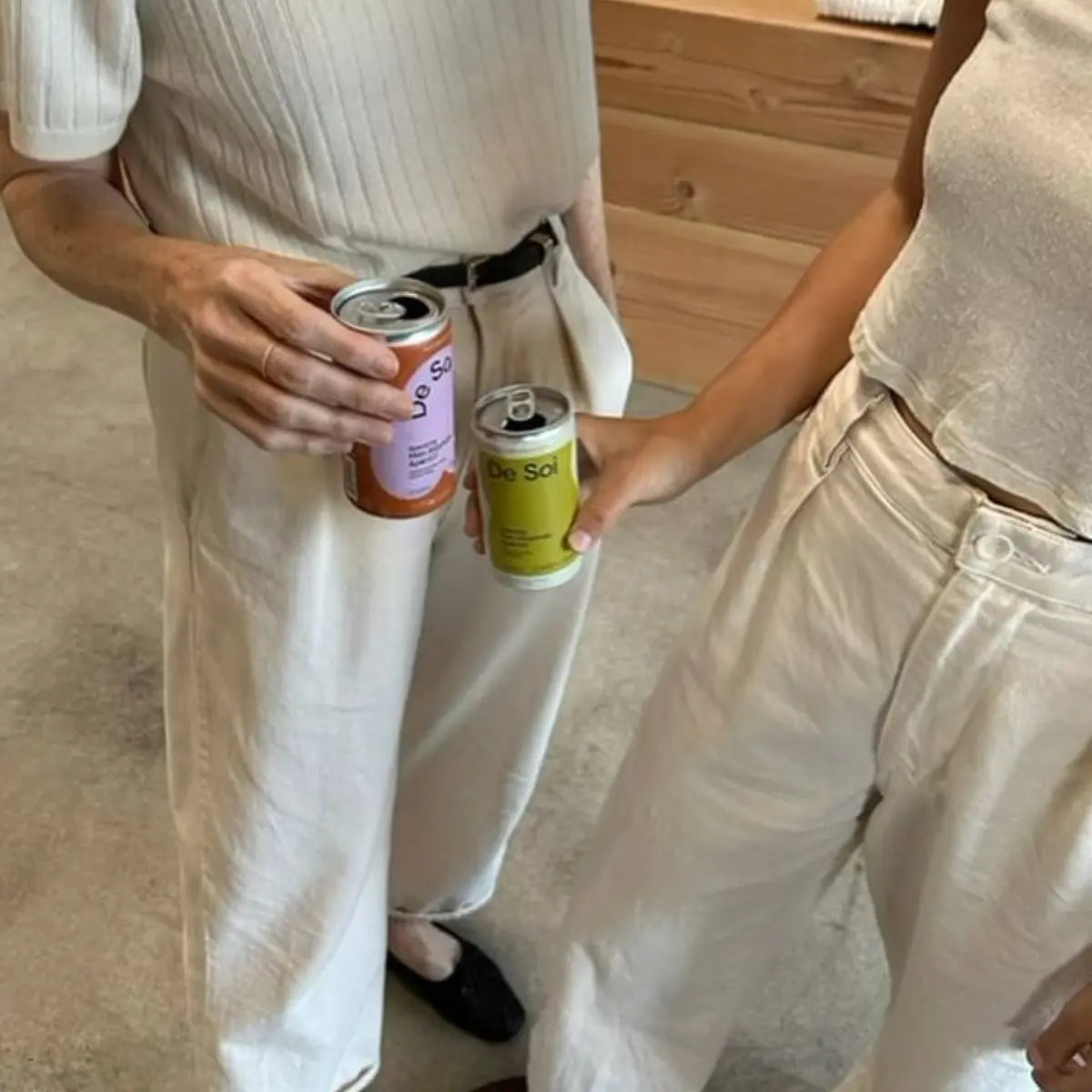 Two people holding cans of adaptogen drinks, both dressed in light, casual clothing.