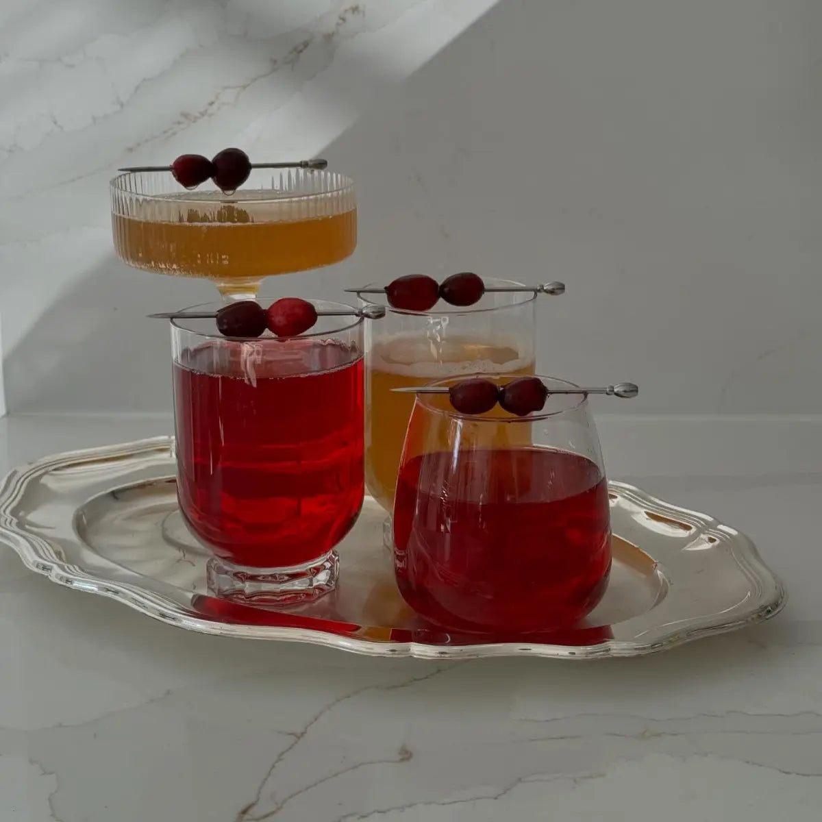 Mocktail beverages garnished with cranberries served on an elegant silver tray with soft natural lighting.
