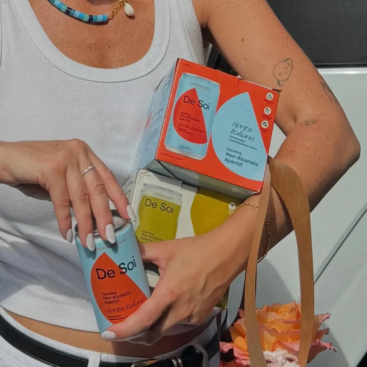 Person holding a De Soi Spritz Italiano non-alcoholic aperitif can beside packaged boxes.