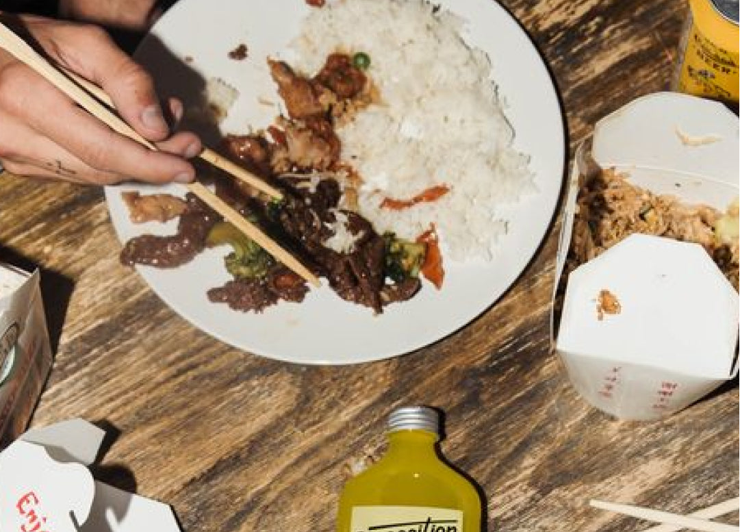 Chinese takeout with chopsticks over rice, paired with a non alcoholic aperitif bottle.