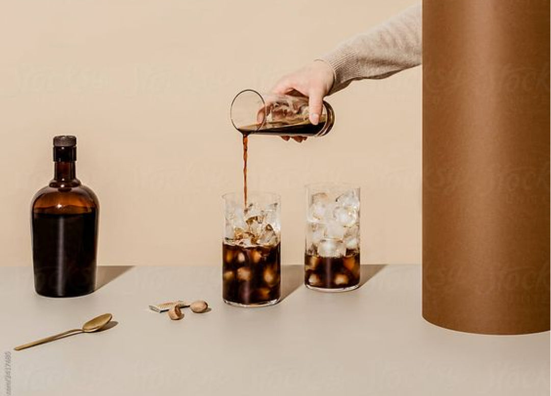 Pouring a dark non alcoholic cocktail over ice beside an amber apothecary bottle.