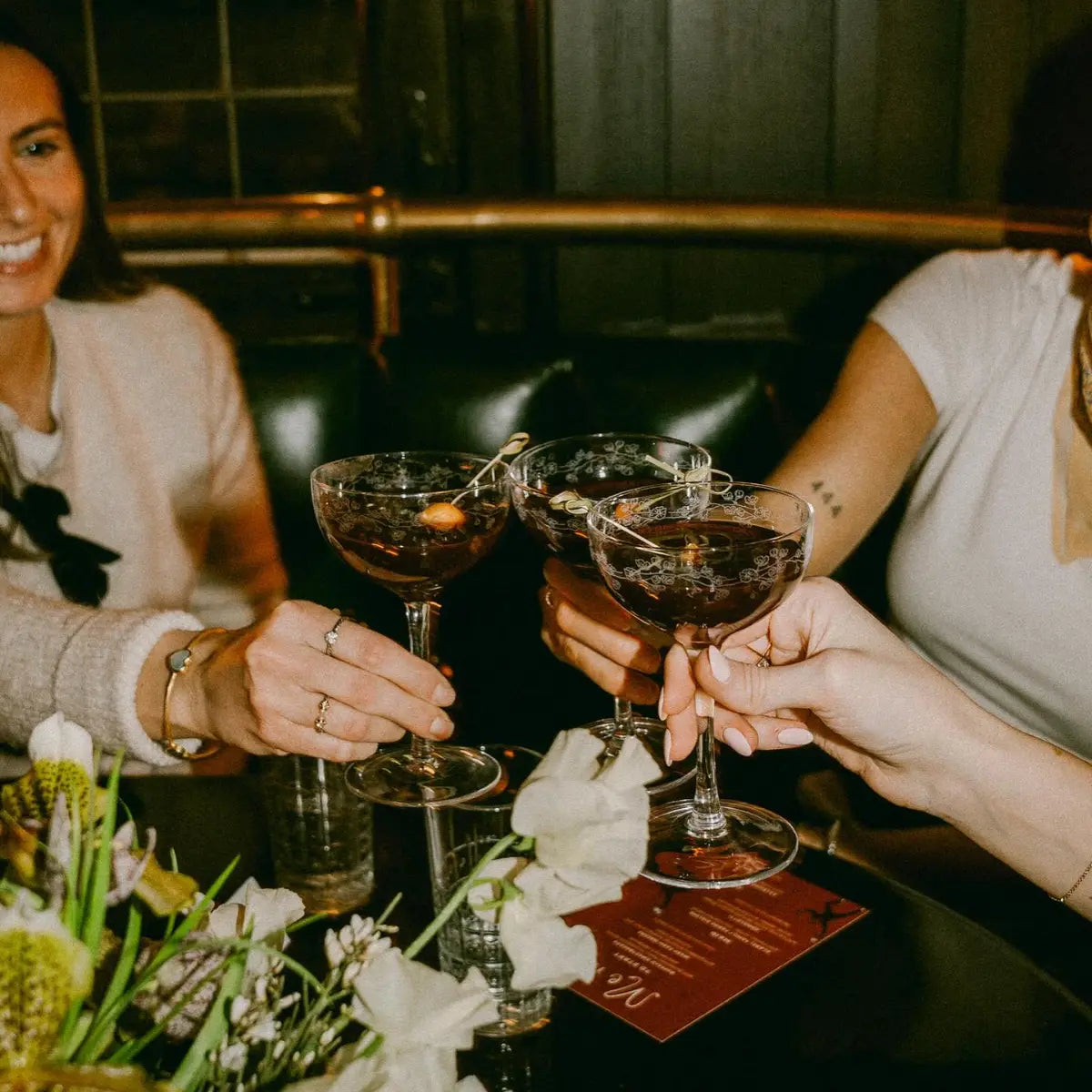 Alcohol-free drinks served in elegant coupe glasses as friends toast in a dimly lit lounge setting