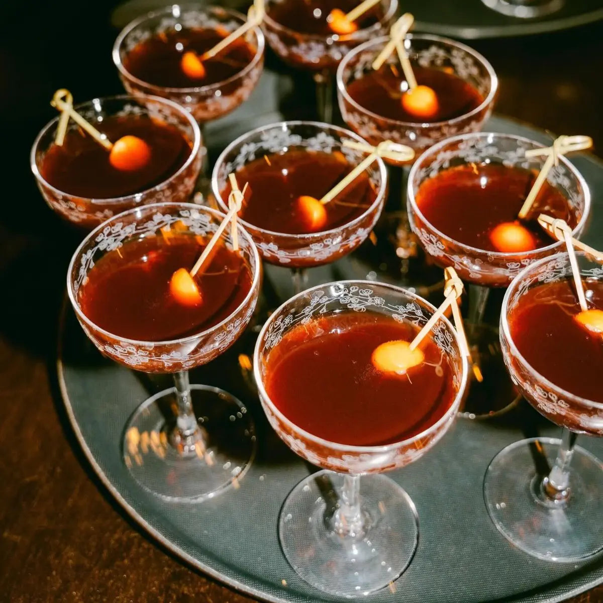 Aperitif drinks without alcohol served in elegant coupe glasses with skewered garnishes on a tray.