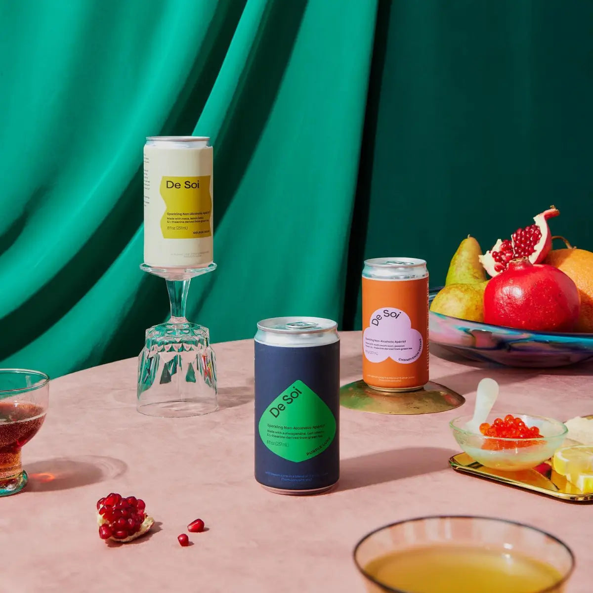 Best non-alcoholic cocktails from De Soi displayed on a table with fruits and snacks against a green fabric backdrop.