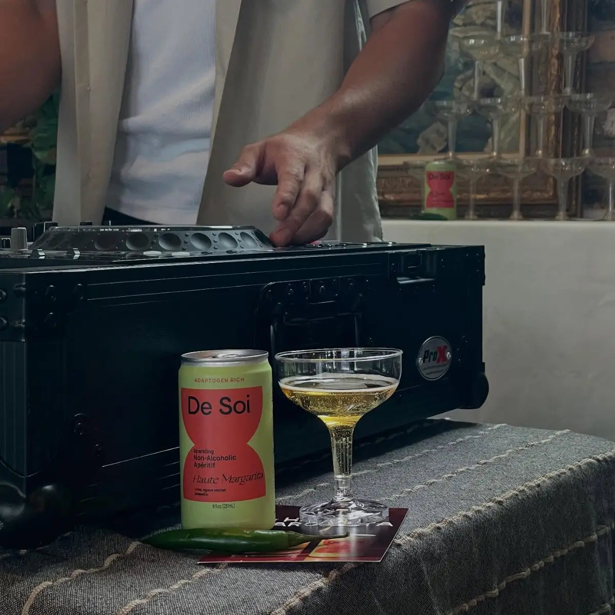 Fancy mocktails and a De Soi can placed beside a DJ booth during a lively indoor gathering