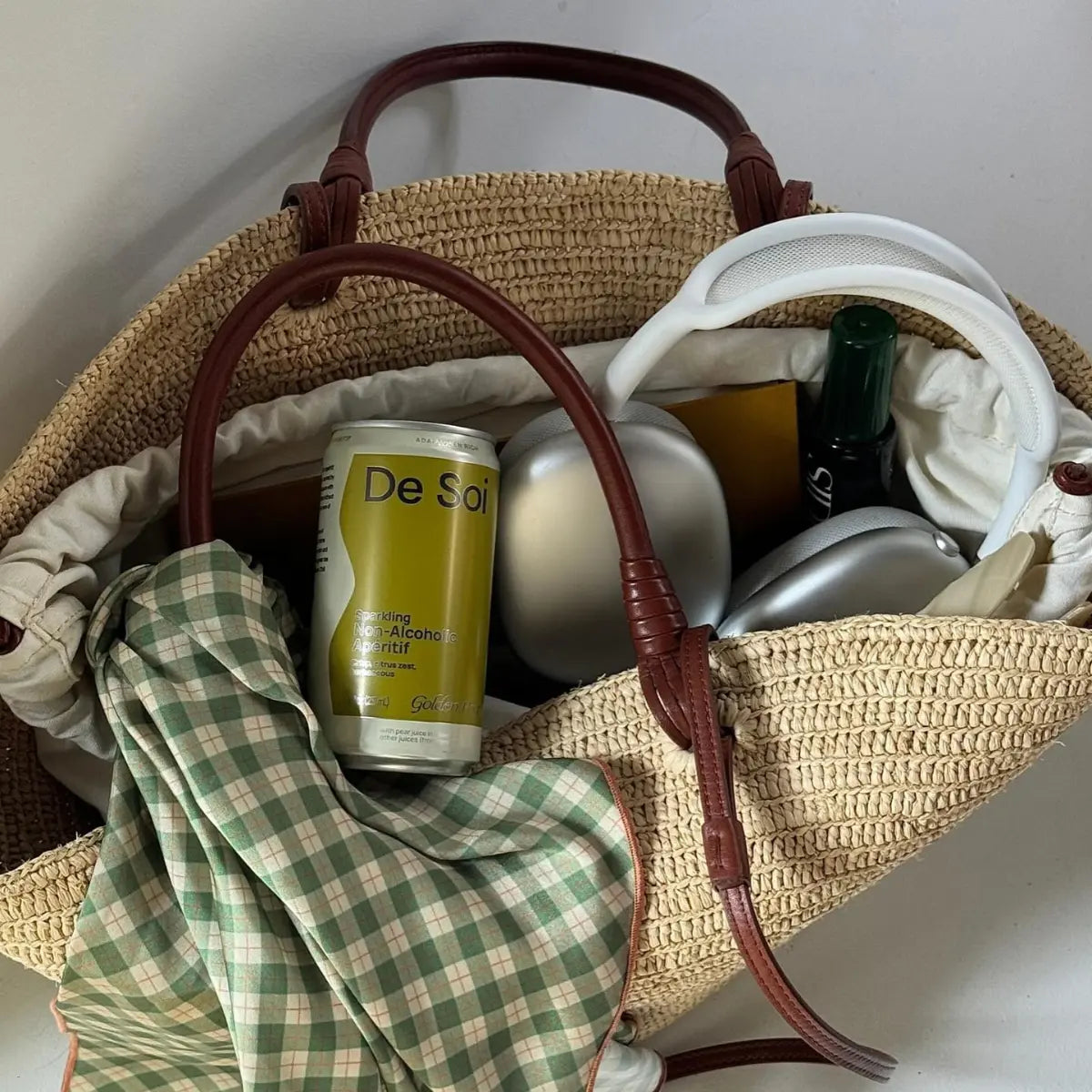 Floral mocktail with De Soi Golden Hour tucked in a woven spring bag with headphones and gingham scarf