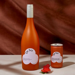 Herbal aperitif with no alcohol in De Soi bottle and can, placed with fresh strawberries on a burgundy backdrop