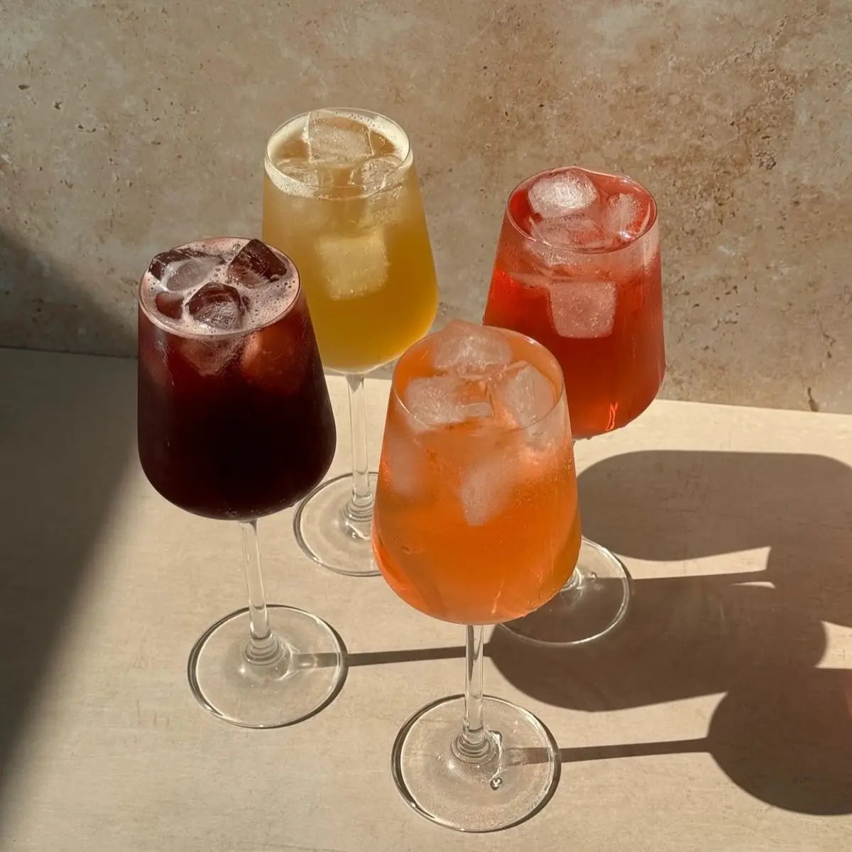 Mocktails with adaptogens served in wine glasses with ice, featuring a colorful variety under natural sunlight.