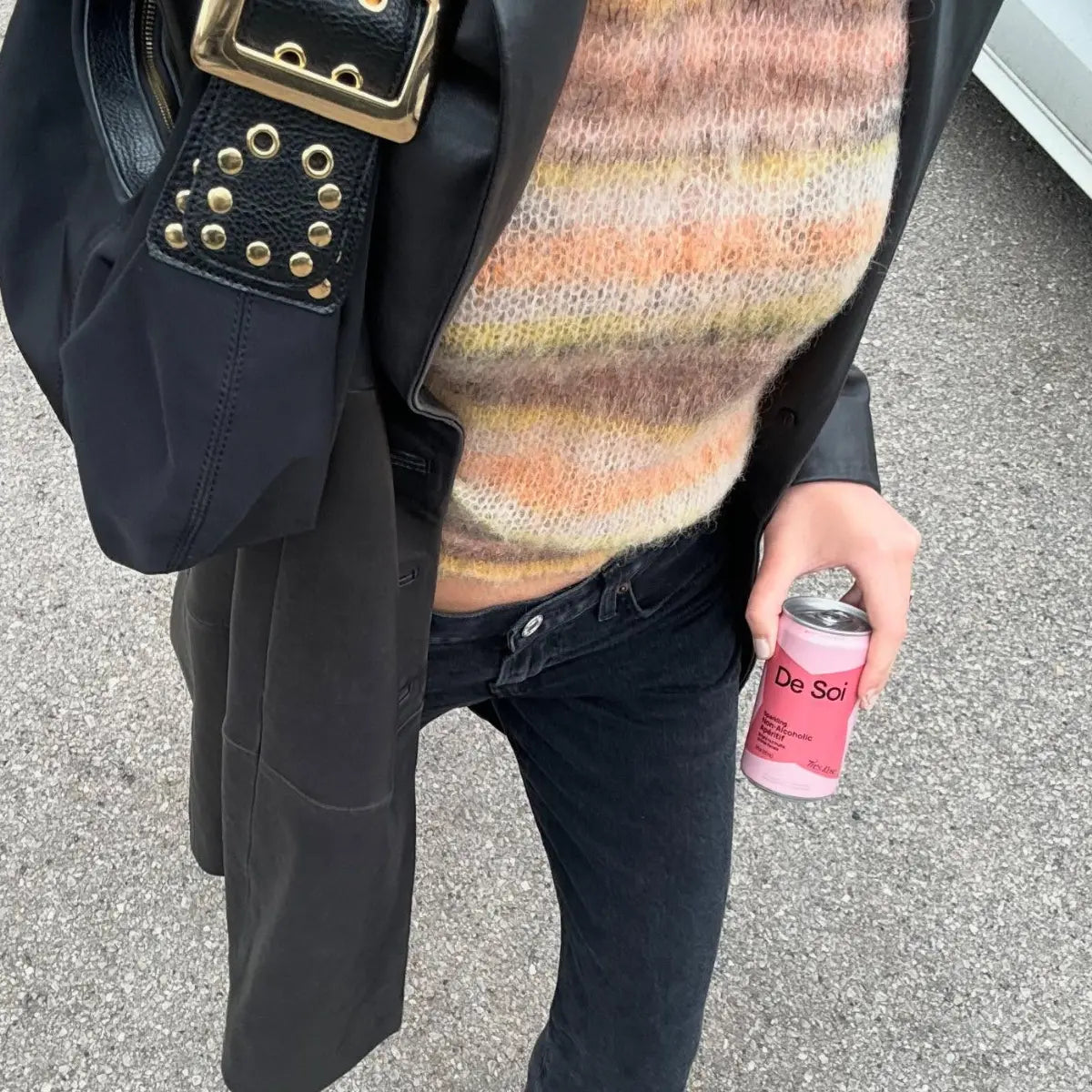 Wellness drink in a pink De Soi can held by a stylish person in a fuzzy sweater and leather jacket
