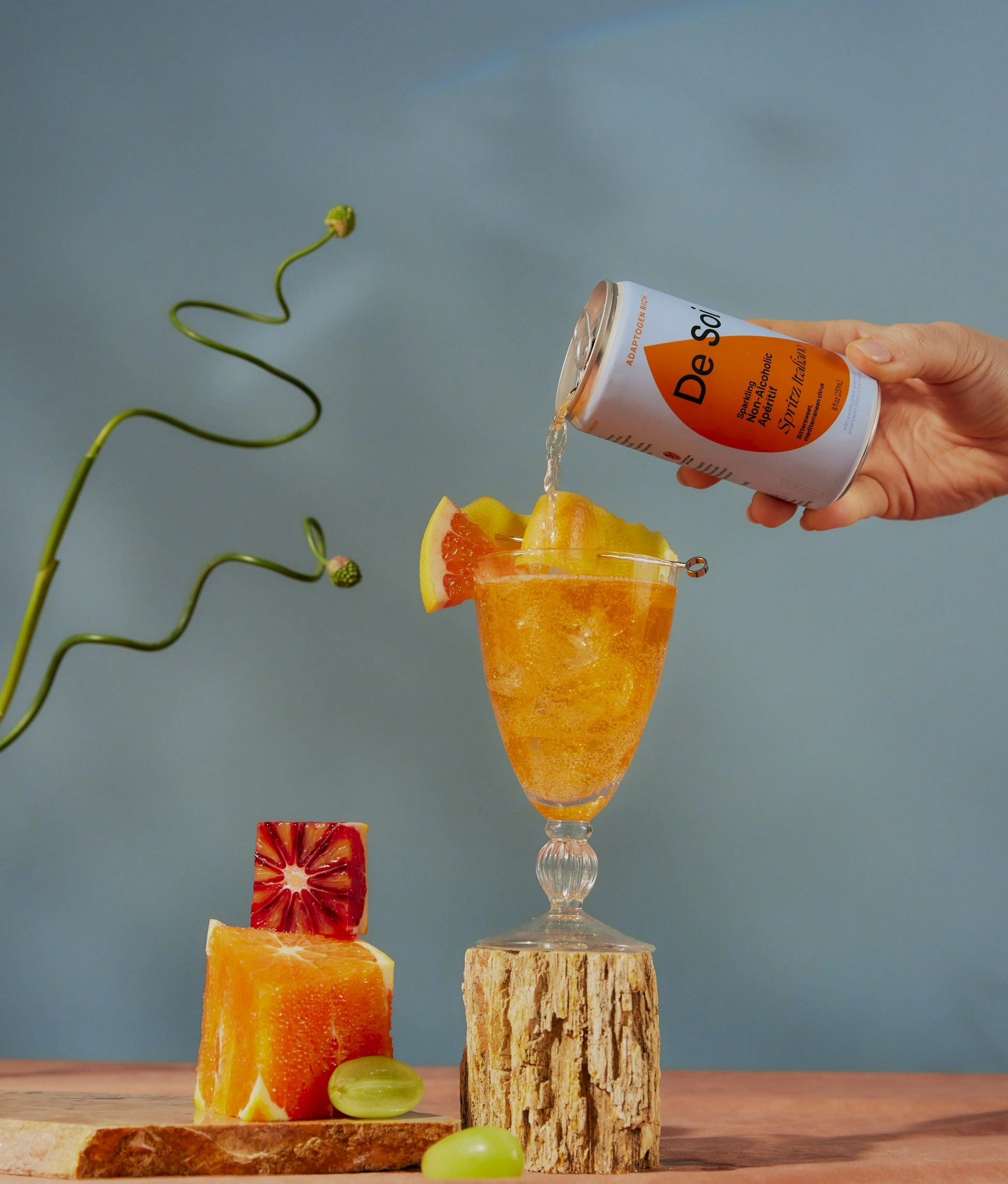 Hand pouring De Soi Spritz Italiano non-alcoholic aperitif over ice with citrus garnish.