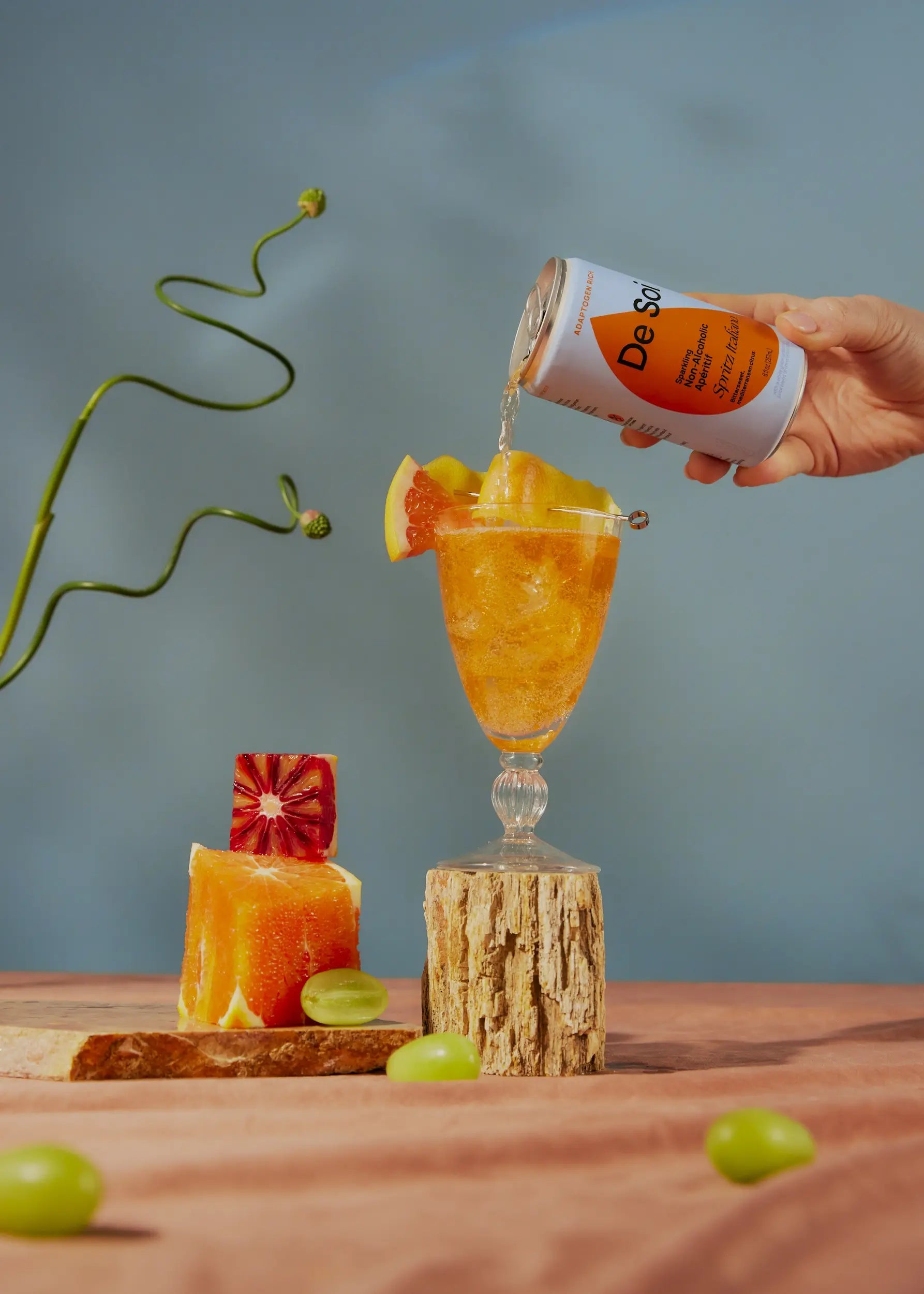 Hand pouring De Soi Spritz Italiano non-alcoholic aperitif over ice with citrus garnish.