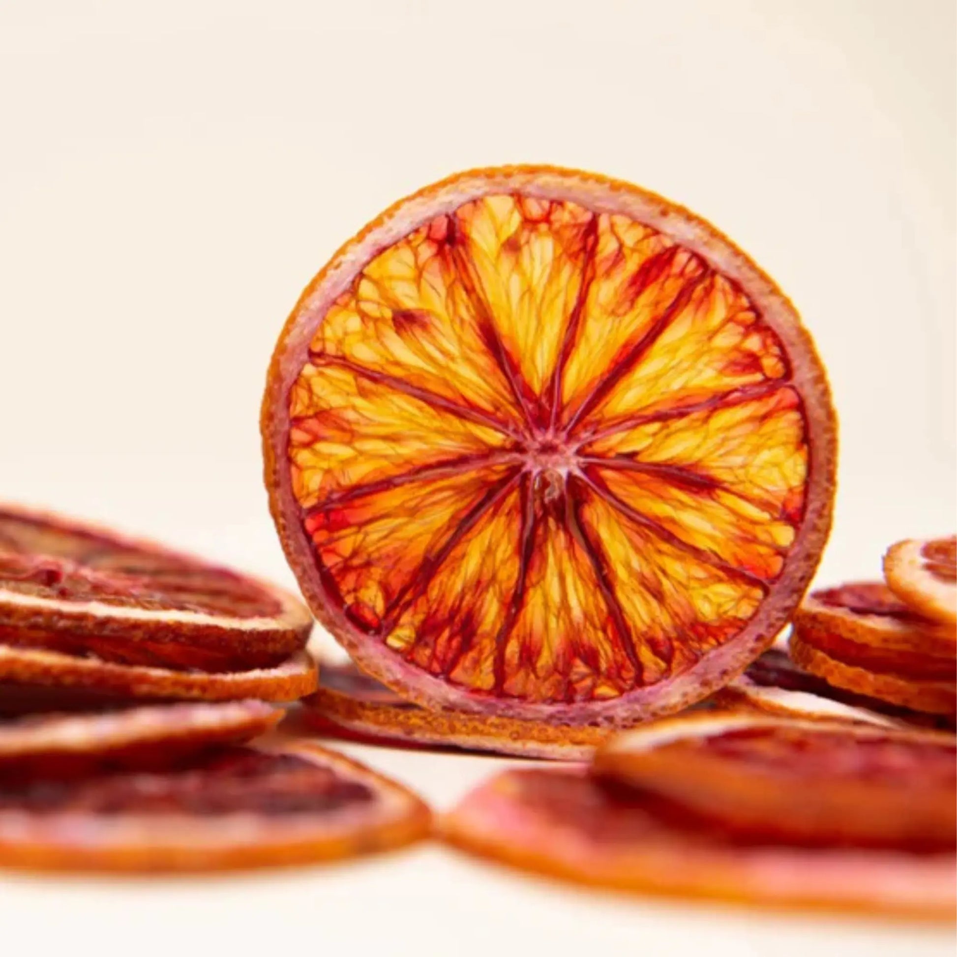 Close-up of dried blood orange slices with vibrant red and orange patterns on a light beige background.