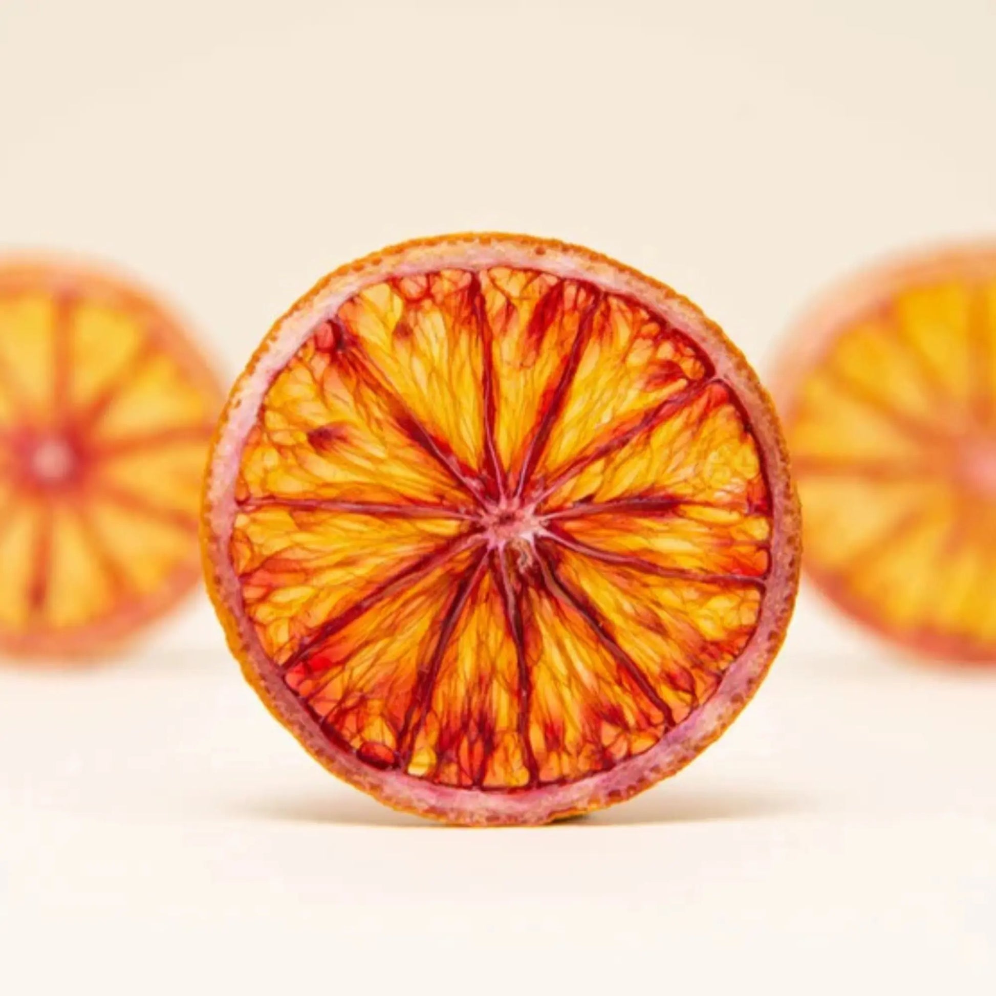 Single dried blood orange slice displayed against a light beige background with partial slices on each side.
