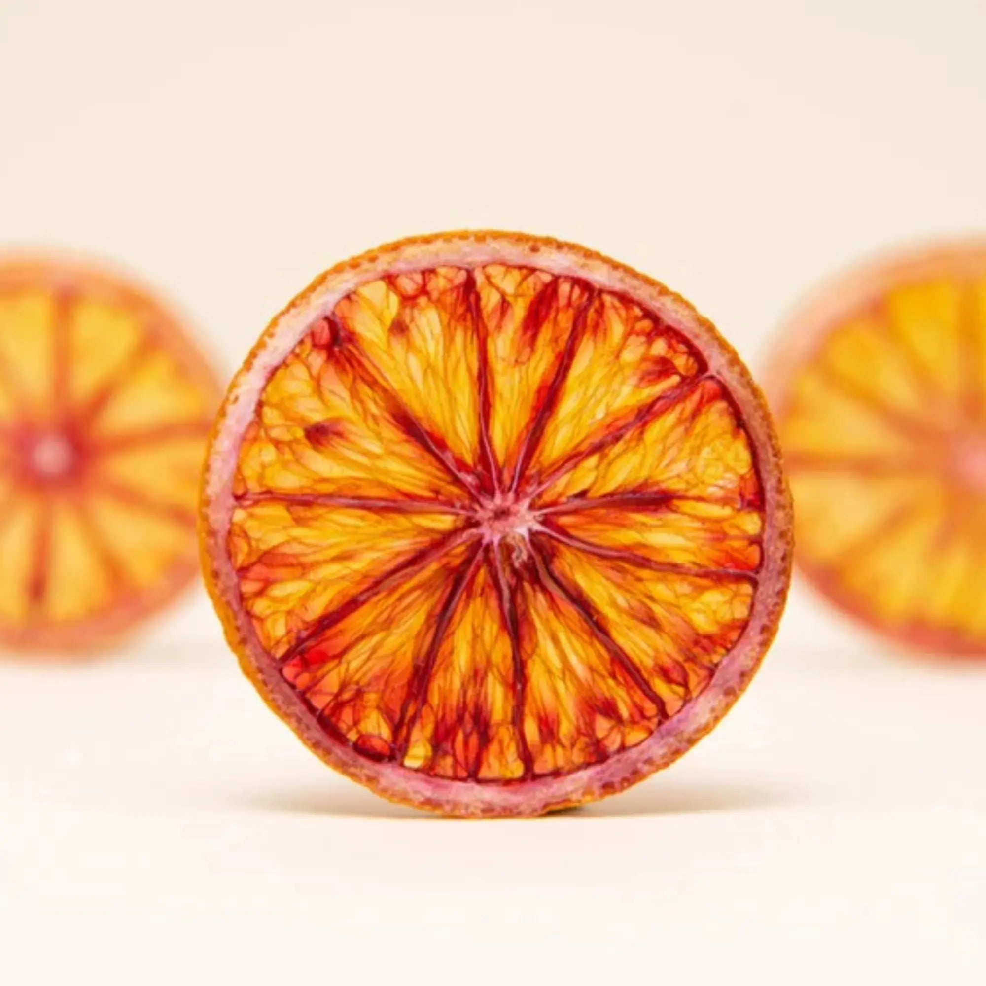 Single dried blood orange slice displayed against a light beige background with partial slices on each side.