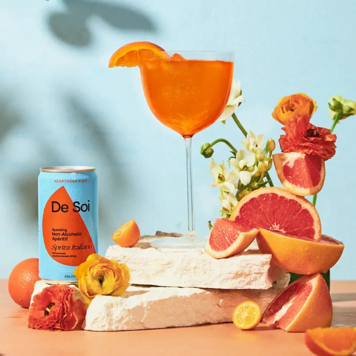 De Soi Spritz Italiano non-alcoholic aperitif can beside an orange spritz with citrus and flowers.