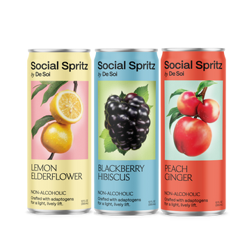Three cans of Social Spritz by De Soi in Lemon Elderflower, Blackberry Hibiscus, and Peach Ginger, non-alcoholic adaptogen drinks lined up in a row.