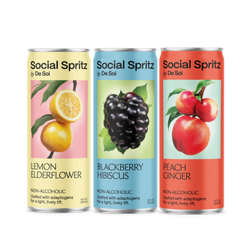 Three cans of Social Spritz by De Soi in Lemon Elderflower, Blackberry Hibiscus, and Peach Ginger, non-alcoholic adaptogen drinks lined up in a row.