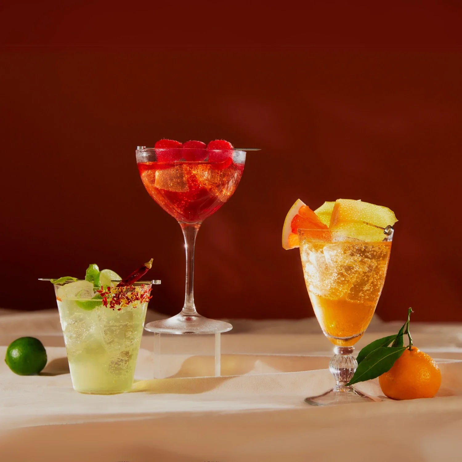 Three De Soi non-alcoholic cocktails garnished with citrus, raspberries, and lime on a warm backdrop.